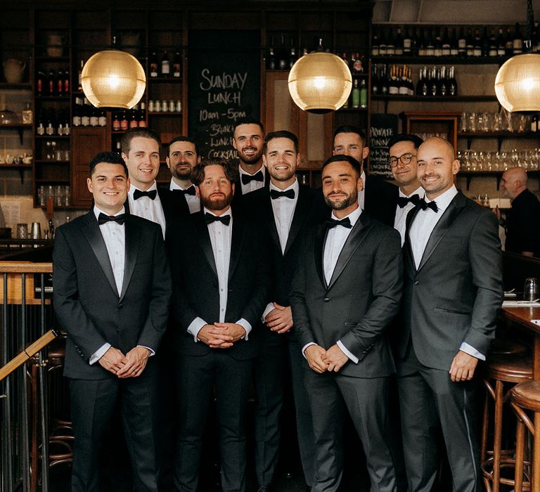 The groom and groomsmen pose together al wearing black tuxedos for classic wedding 