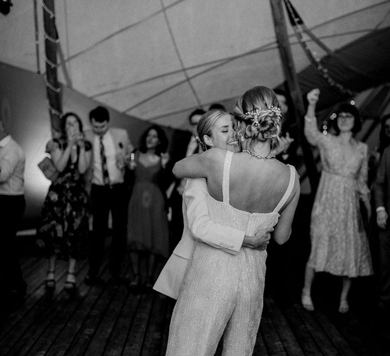 Bride in suit dancing with the bride in a sequin jumpsuit at tipi wedding reception 