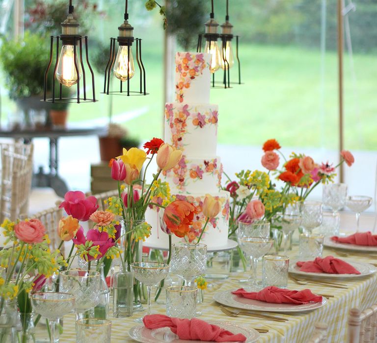 Four tier white iced wedding cake with painted pink, orange and green floral design 