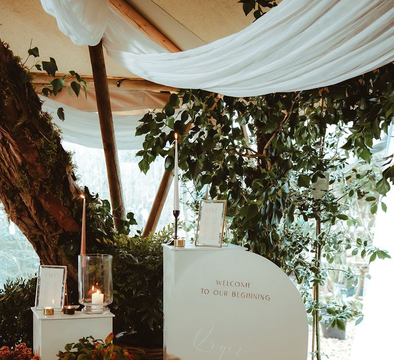 Wedding welcome signage with foliage and candles and gold photo frames with wedding table number sign 