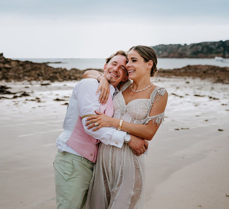 Bride wearing sparkly corset wedding dress with groom in pink waistcoat on the coastal beach wedding 