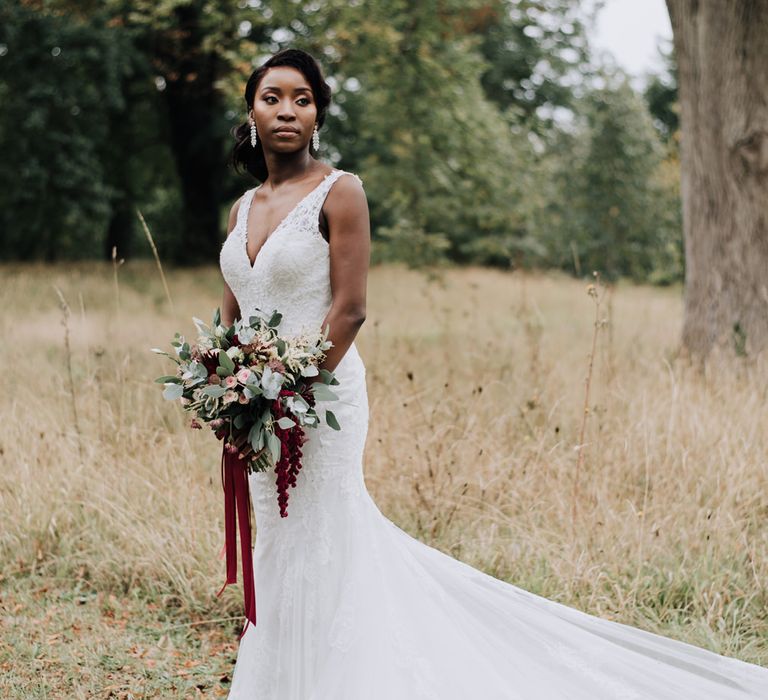 Beautiful bride in a lace fishtail wedding dress holding a burgundy and green wedding bouquet 