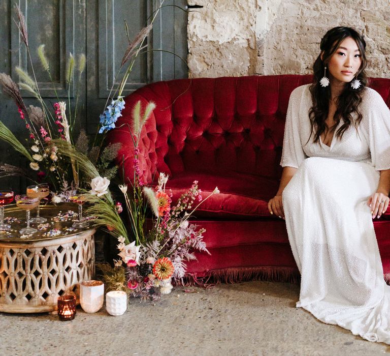 Asian bride in a white sparkly wedding dress sitting on a red velvet sofa 