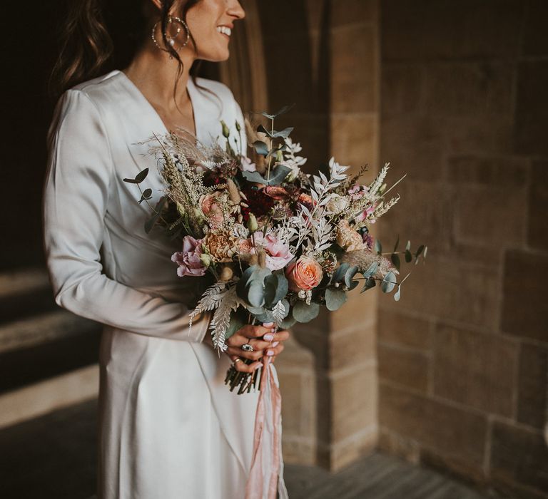 Bride in wrap wedding dress carrying pastel bouquet with green foliage 