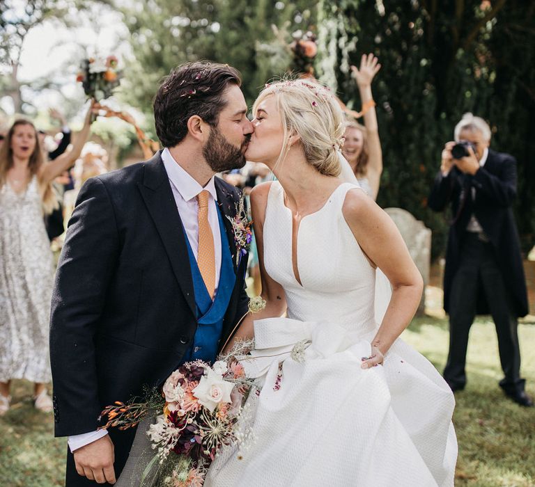 Bride and groom kissing at the end of the confetti line 