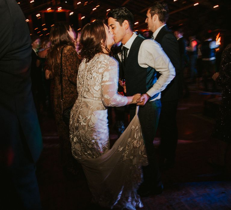 Bride in a lace Hermione de Paula wedding dress with long sleeves and button back detail kissing her groom on the dance floor 