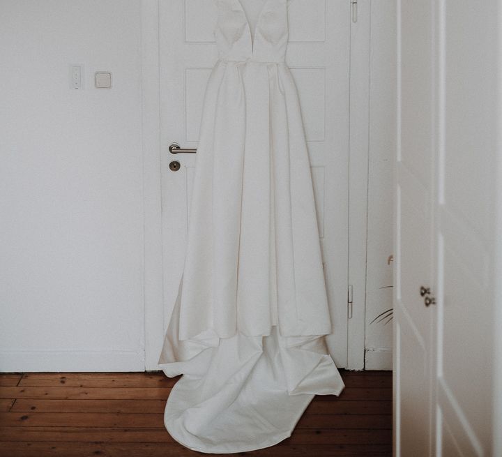 White deep V necked Jesus Piero wedding gown hanging on bedroom door