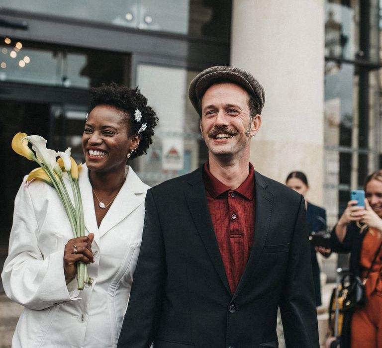 West African bride in a short wedding dress holding a Calla Lily bouquet and her Franco-American grooms hand outside their town hall wedding 