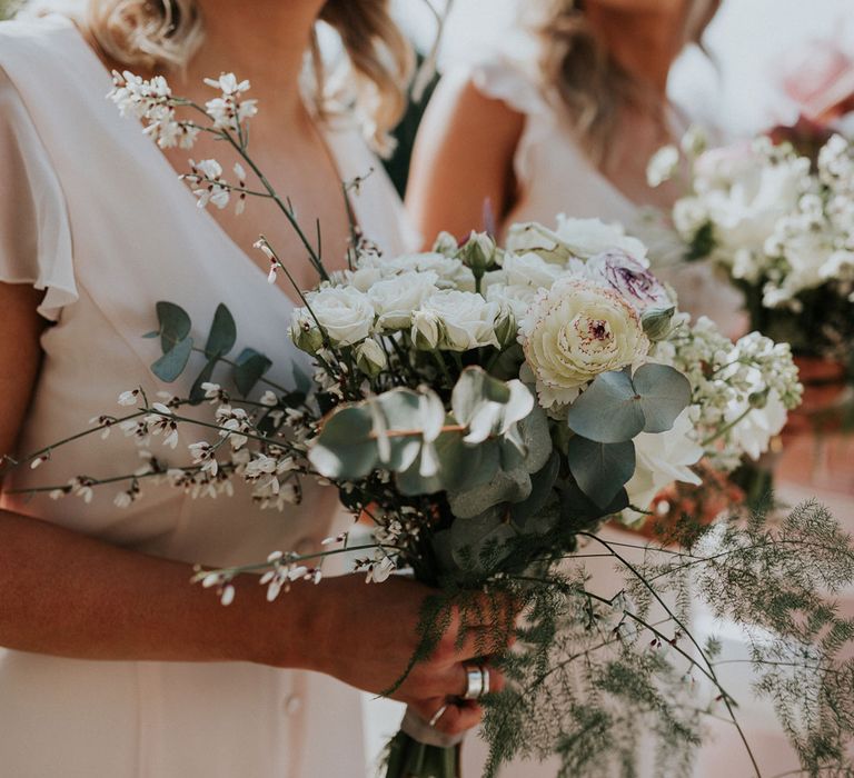 Bridesmaids in silk ivory button bridesmaids dress hold white rose, ranunculus and fern bouquets at Caswell House wedding