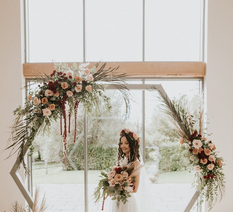 Boho bride in an ASOS wedding dress holding an oversized bouquet standing in front of a wooden altar 