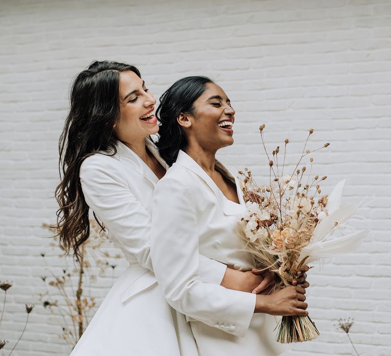 Brides hugging with dried flower bouquet at all white luxe industrial wedding shoot