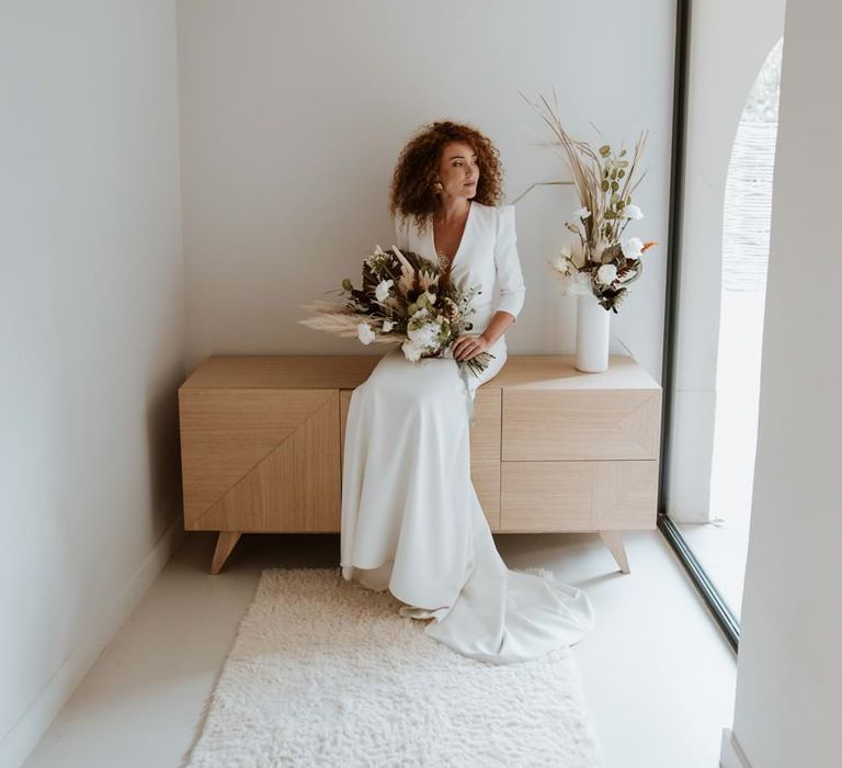 Bride sitting in minimalist wedding theme venue with sculptural bouquet