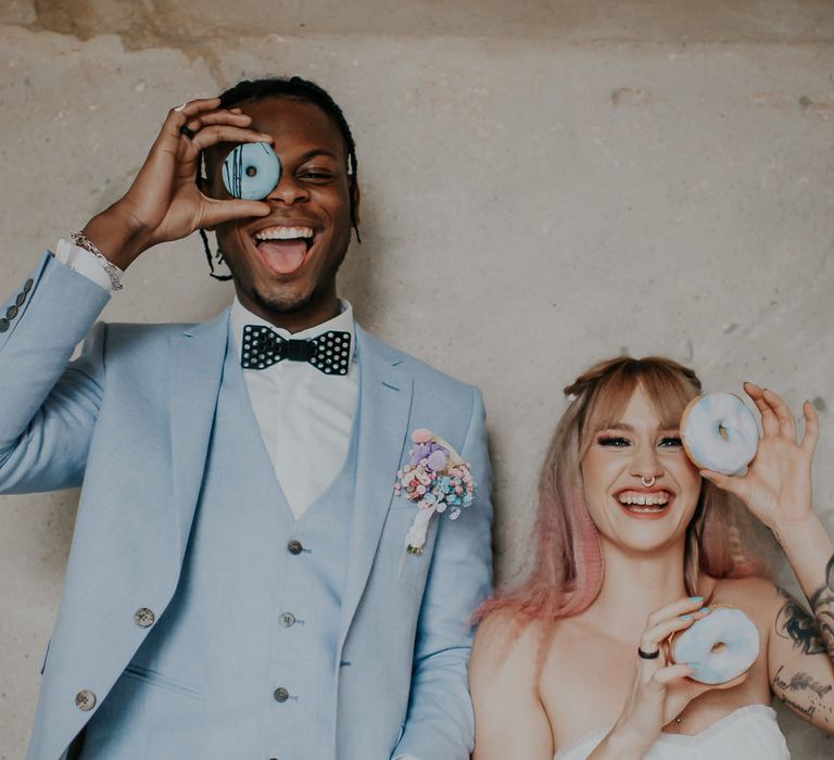 Bride and groom standing at the dessert table having fun with the doughnuts 