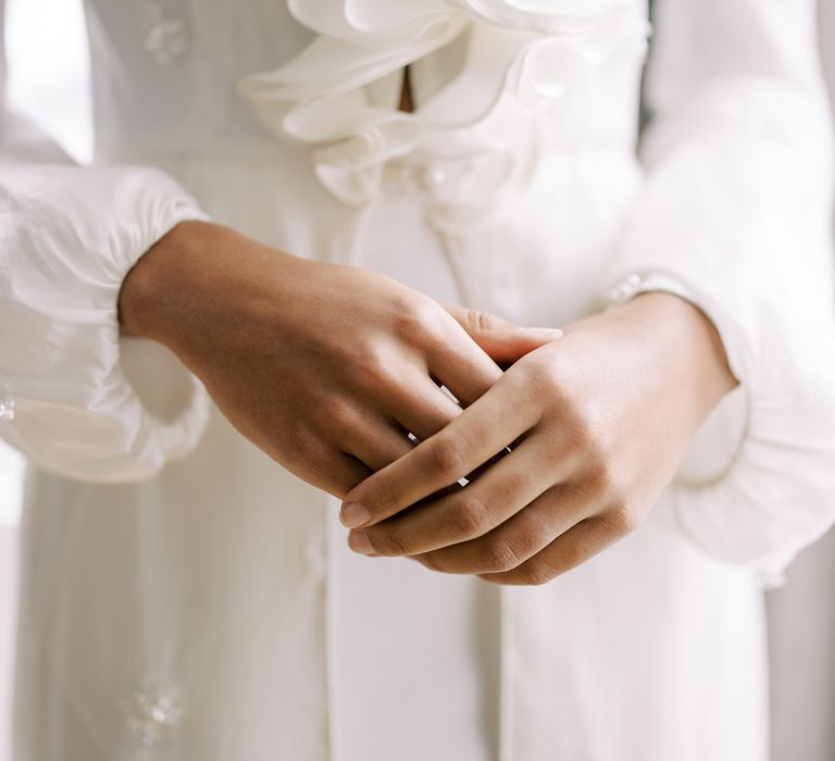 Bride clasps hands together whilst wearing long sleeved bridal gown with full sleeves and ruffled front