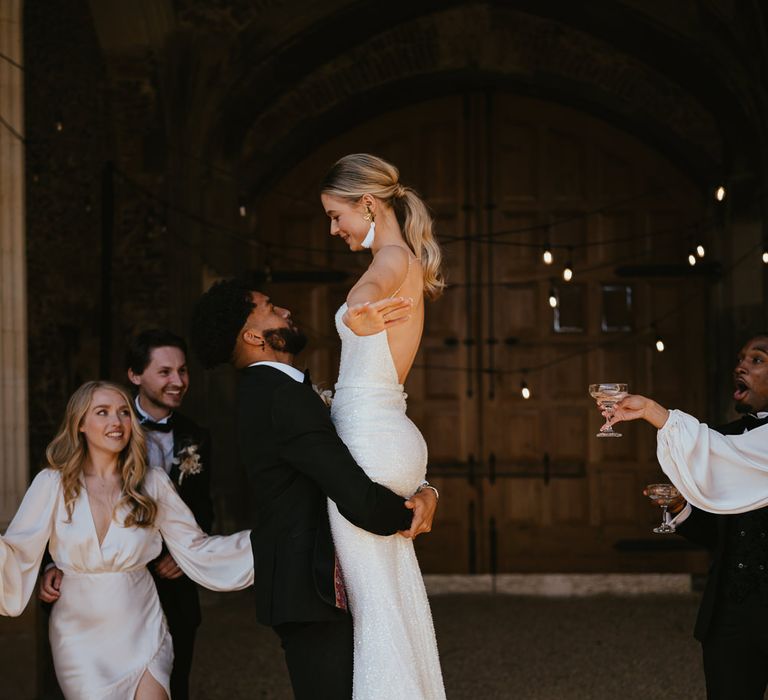 Groom in a tuxedo picking up his bride in a fitted sparkly wedding dress at Pentney Abbey Estate