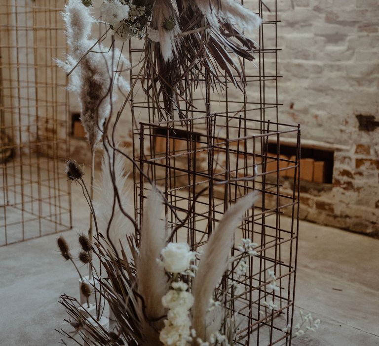 A metal structure forms a wedding altar. It is decorated with dried flowers and grasses in neutral tones for a simple elegant wedding. 