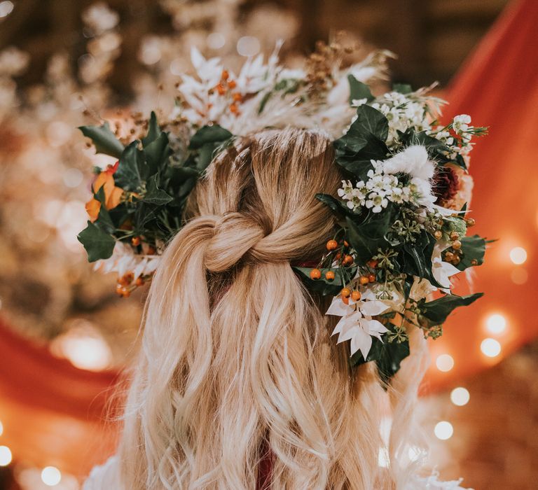 Bride wearing a large flower crown made of ivy, orange berries and white flowers for pumpkin spice wedding, her hair is in a half up/half down style with a loose knot