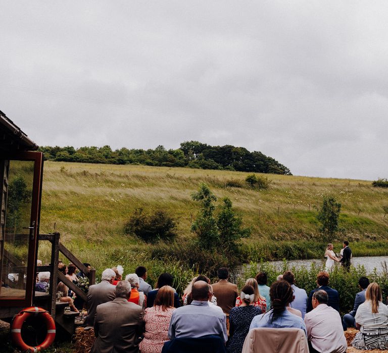 Wedding guests sit together as they look across the lake before wedding ceremony