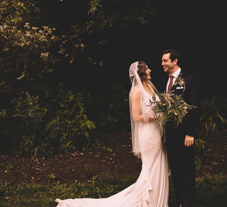 Bride and groom portrait with bride in a Juliet wedding veil holding a blue thistle and green foliage bouquet 