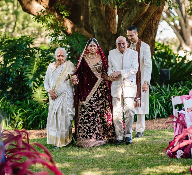 Bride walks down the aisle in her traditional lehenga surrounded by her family on her wedding day