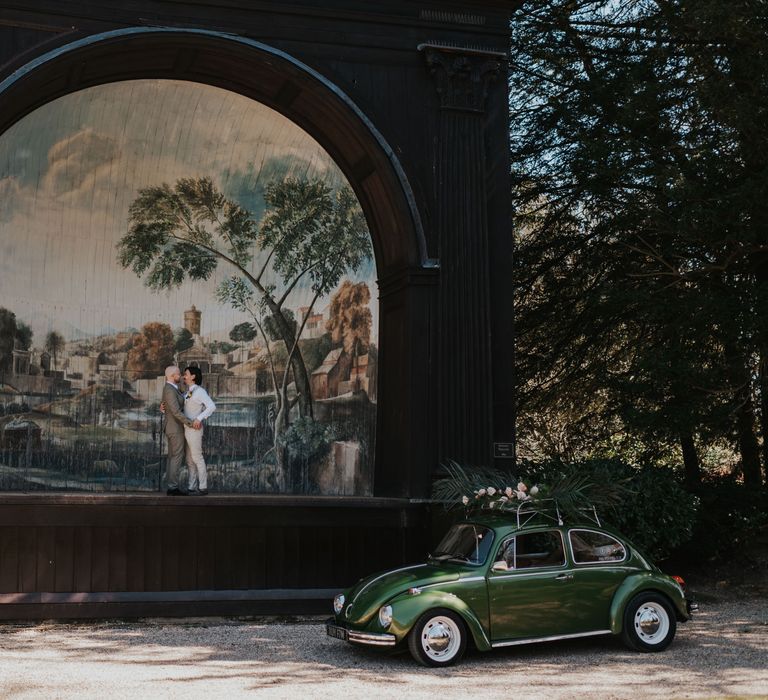 Two groom standing on the Larmer Tree Gardens bandstand with a green beetle wedding car 