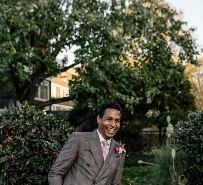 Stylish groom in a checked charcoal grey wedding suit leaning up against the wall