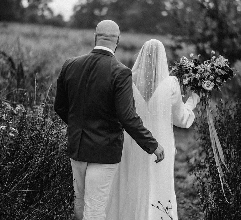 Bride & groom walk together across fields in black & white image