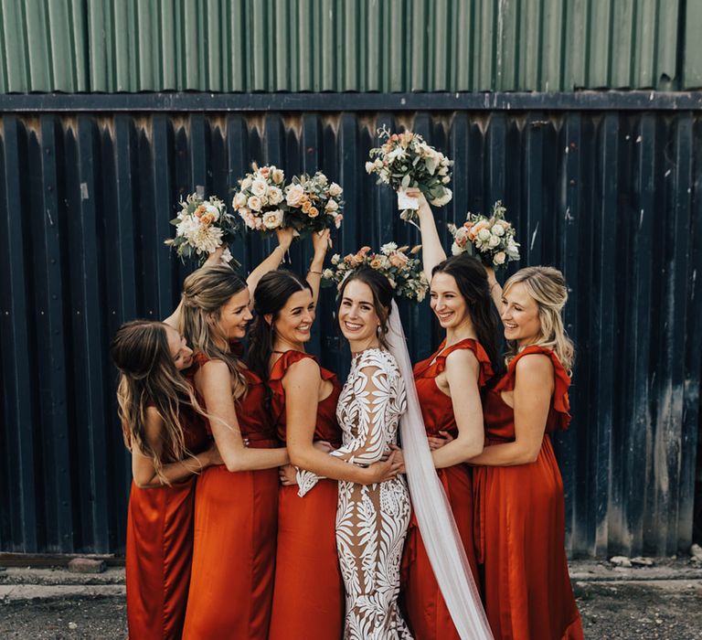 Bridal party with milk churn flower arrangement in the air & silk orange bridesmaid dresses stand with Boho Bride 