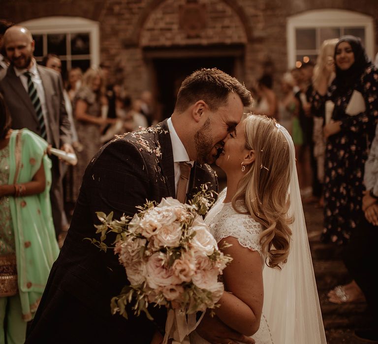 Confetti moment at Dewsall Court with bride in a lace cap sleeve wedding dress holding a pink rose bouquet 