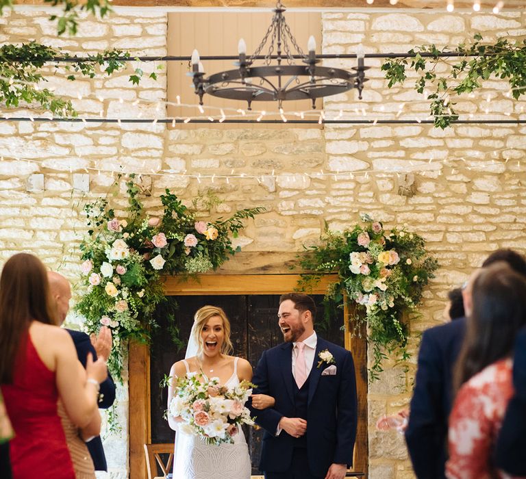 Bride in an embellished wedding dress and groom in a navy suit standing at the altar of their Caswell House wedding with fairy lights and spring flower decor 