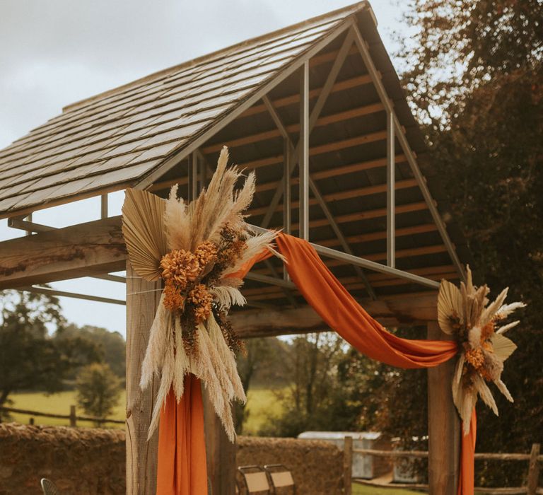 Outdoor wedding ceremony in Dorset with orange draping, pampas grass installation and rustic aisle decor