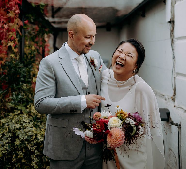 Bride & groom laugh with one another on their wedding day outdoors 