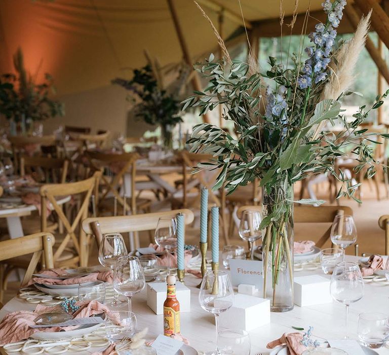 Pastel themed tables cape with twisted blue candles, gold and silver accents, pink napkins, tall dried flower centrepiece