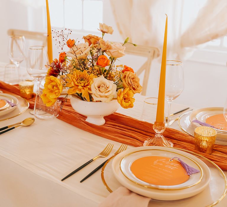 Elegant place setting with orange table runner, taper candles and menu card on gold rimmed plates