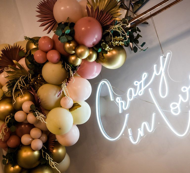 White crazy in love neon sign with balloon decor in pink, yellow, and gold with fan decor