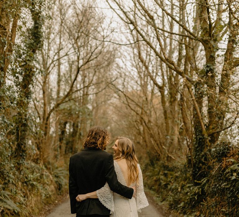 Bride in low back lace wedding dress with bell sleeves and train with groom in black tie for barn wedding