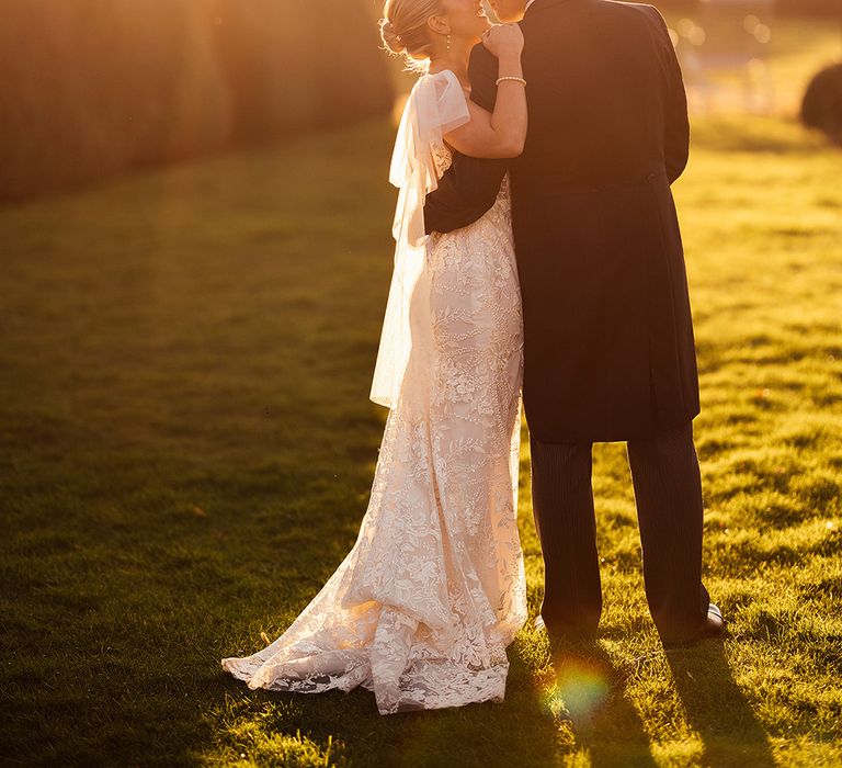 Bride and groom lean in for a kiss during golden hour with bride wearing pearl jewellery