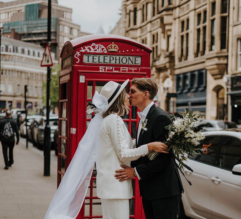 Bride and groom kiss in front of red telephone box 