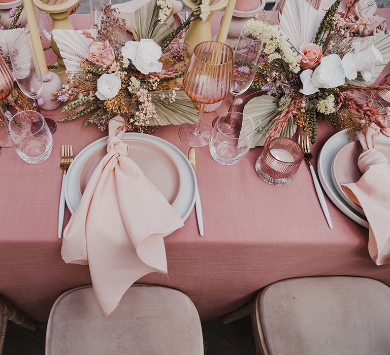 Place setting with pink tablecloth and napkin, pink coloured goblets and preserved pastel flowers and grasses