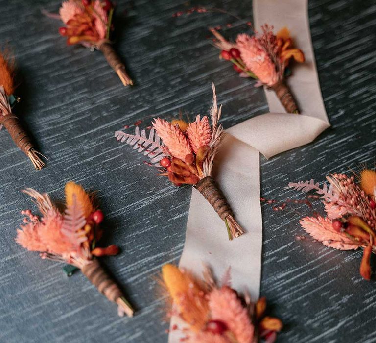 Bright floral buttonholes lay on grey backdrop ready for wedding 