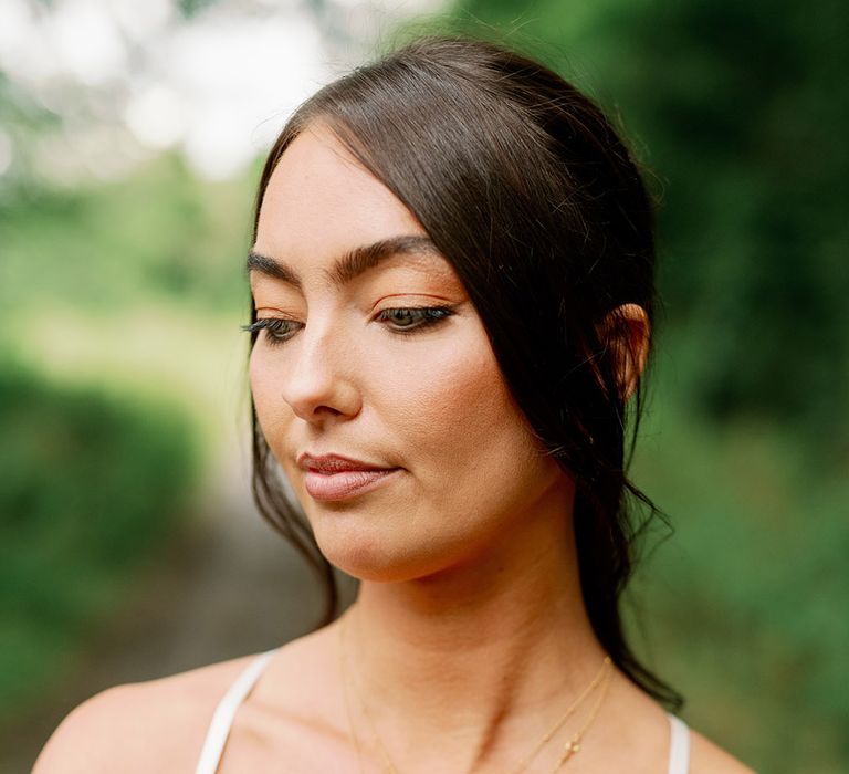 Bride wears her brown hair in low ponytail, white silk slip homemade wedding gown and gold Missoma necklaces 