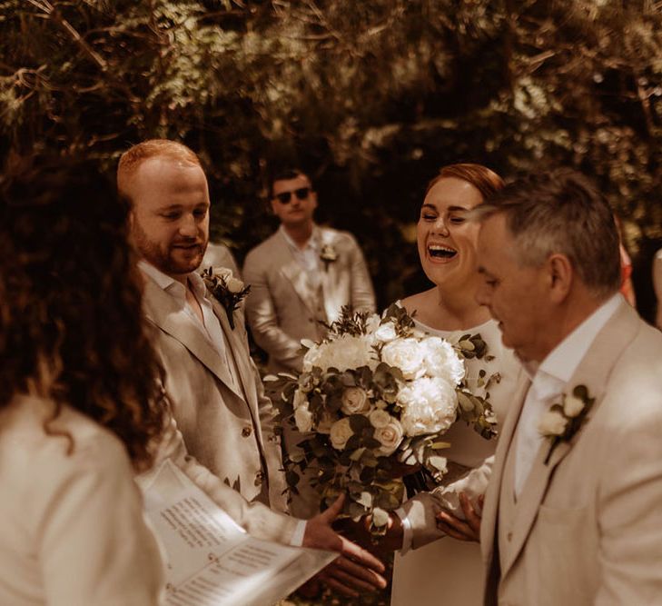 Bride & groom stand at the altar as bride holds white rose floral bouquet 