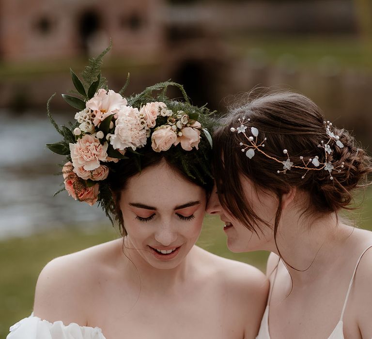 Two brides in ethereal wedding dresses wearing a pink flower crown and gold hair vine bridal accessories 