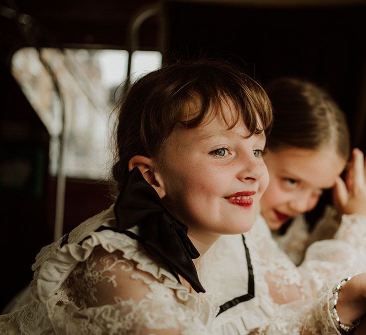 Flower girls wearing lace dresses with black ribbon and red lipstick with their hair tied into plaits 