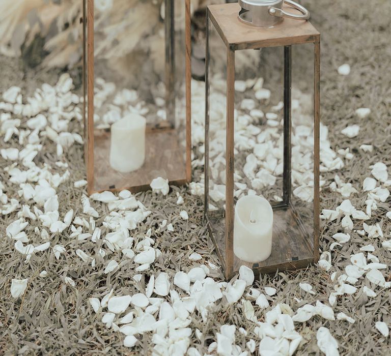 White petals surround glass and wooden cases with white pillar candles for outdoor wedding in Phuket 