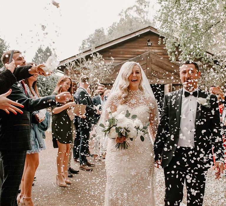 Bride & groom walk through white petal confetti exit outdoors 