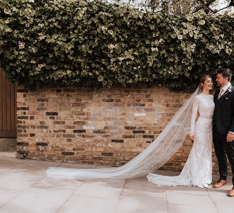 Bride wears floor-length cathedral veil and long sleeve lace wedding dress as she stands with her groom after Hackney Town Hall wedding