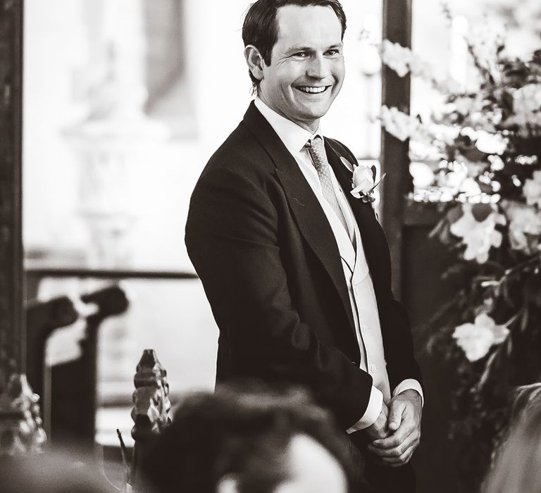 Groom stands smiling at the altar waiting for the bride 