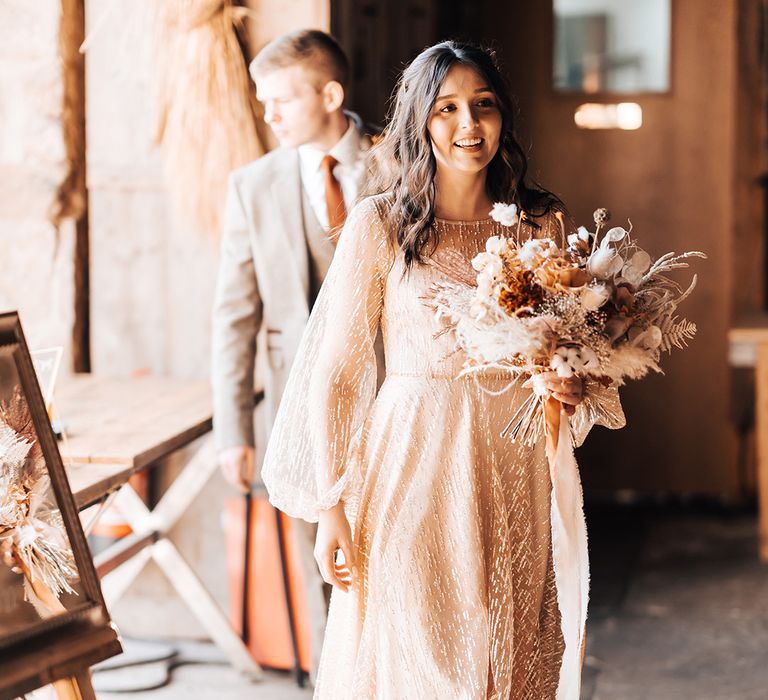 Bride holds dried floral bouquet tied with orange ribbon 