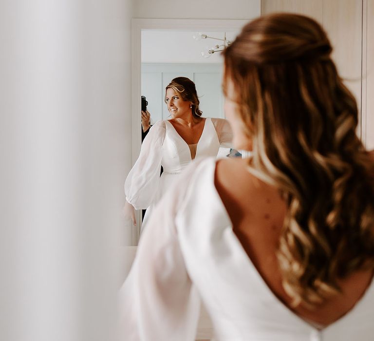 Bride wears sheer full sleeved wedding dress and her hair in loose curls 